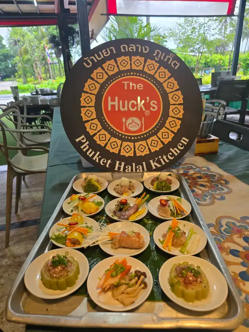 A tray of fusion dim sum on small plates, in front of The Huck's round sign