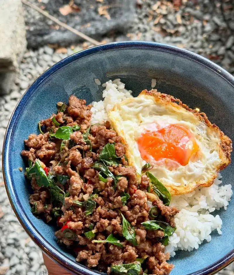 A blue bowl of rice with a holy basil stir-fry and a fried egg