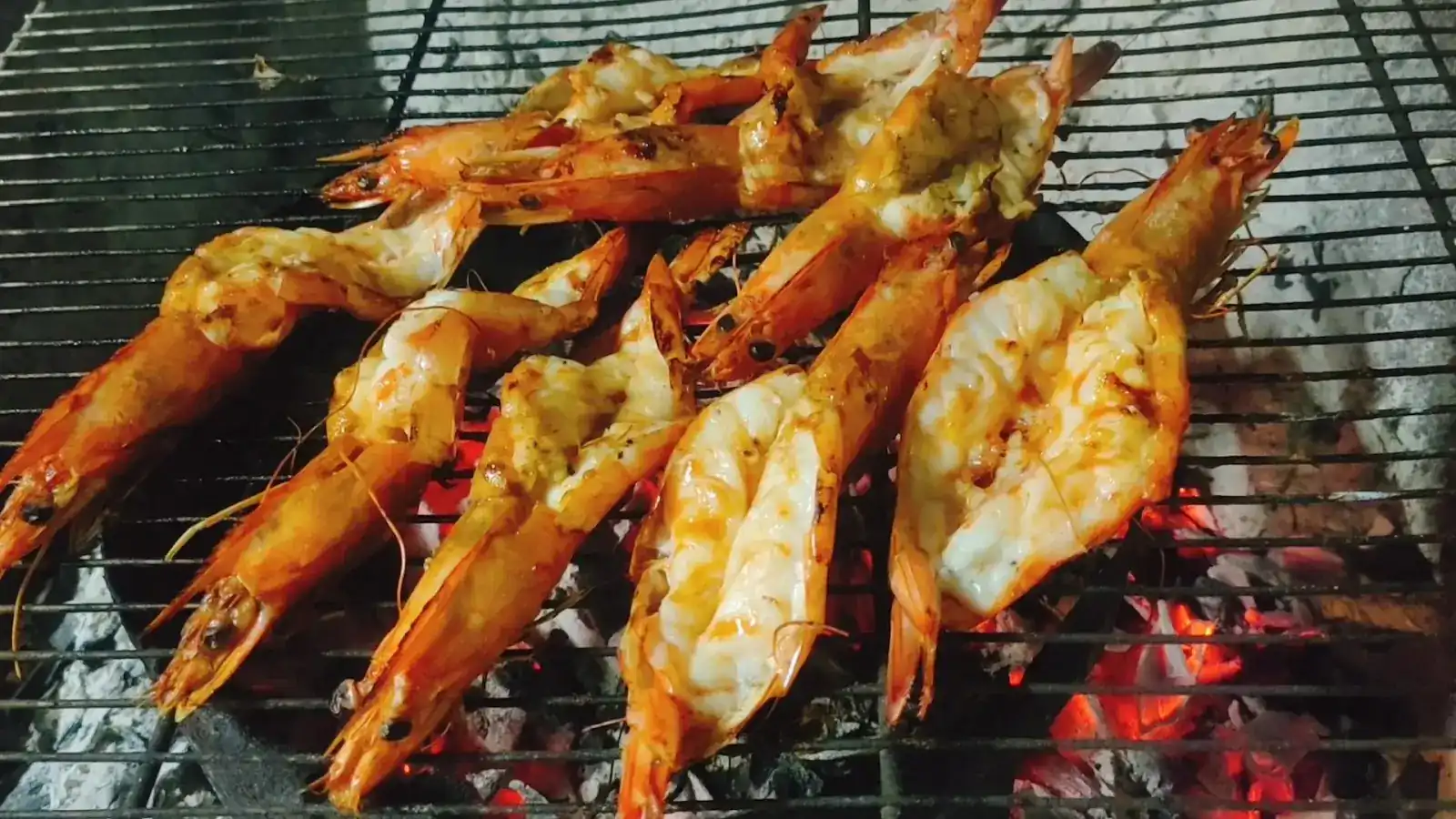 Halved prawns grilling over glowing charcoal