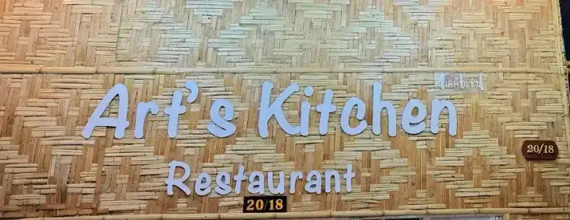 The Art's Kitchen Restaurant sign in white letters on a woven bamboo wall