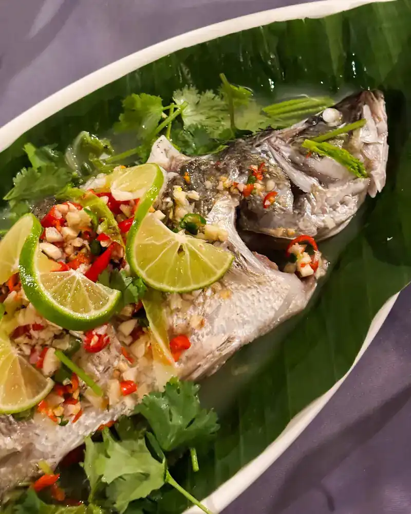 Whole steamed fish with lime slices, garlic and chilli on a banana leaf