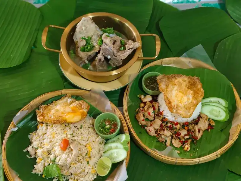 Fried rice and a chilli stir-fry on rice, each with a fried egg, beside a bone soup in a brass pot