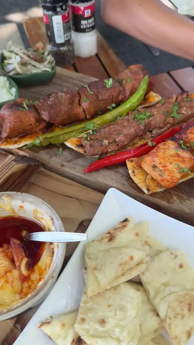 Grilled kebabs and peppers on flatbread, with a red dip and flatbread on the side