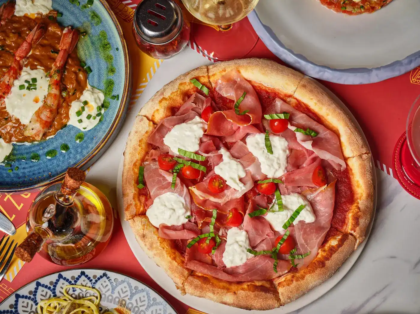 A pizza with ham, fresh cheese, cherry tomatoes and basil on a red paper placemat