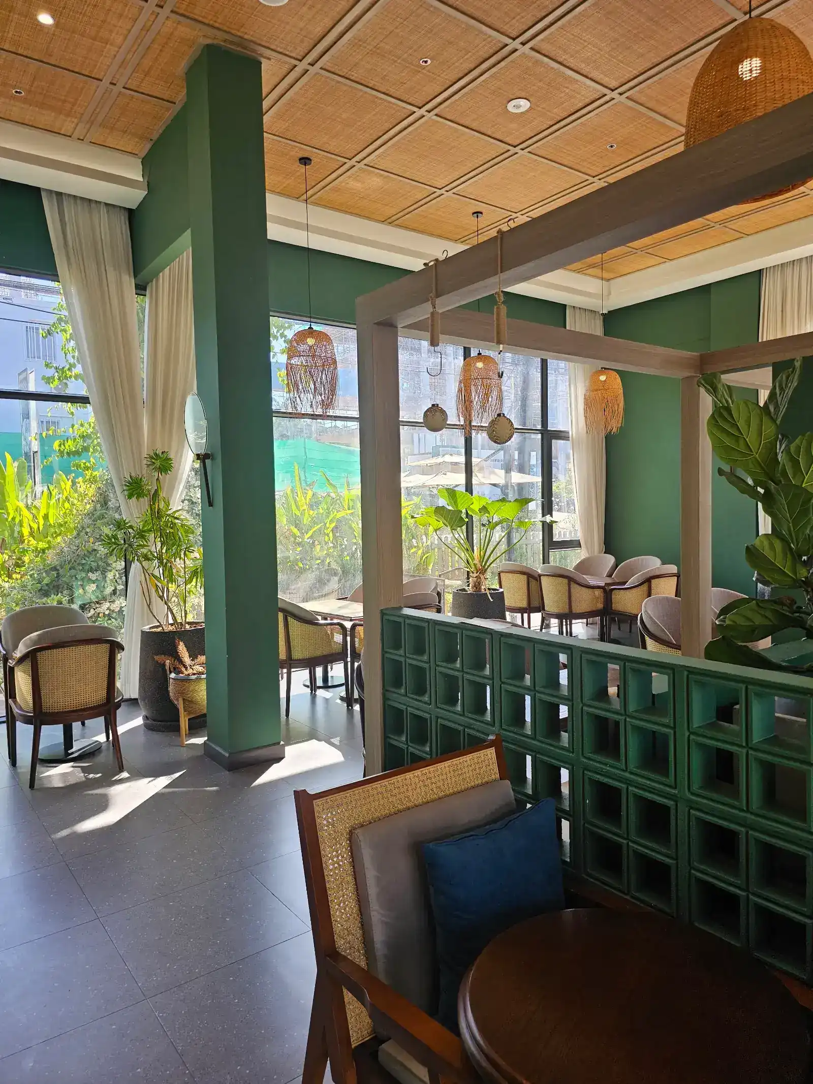 Inside Moodcafé: green walls, a rattan ceiling, woven pendant lamps and cane chairs by tall windows onto the garden