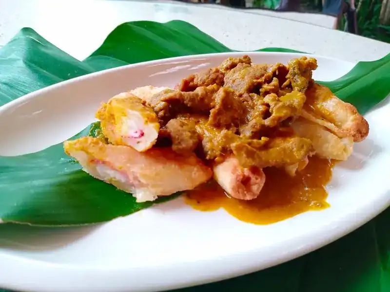 Crisp fried rolls under a thick curry topping, on a leaf