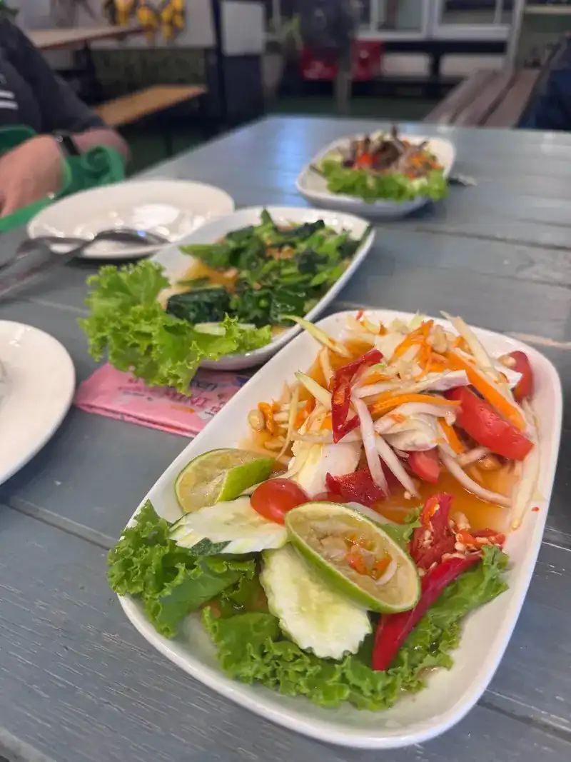 Papaya salad with lime, chilli and fresh vegetables, with a plate of greens behind