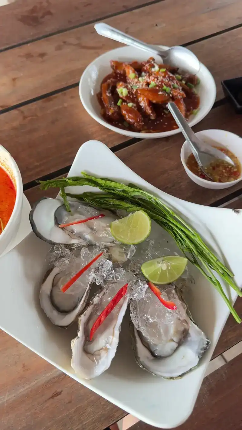 Fresh oysters on ice with lime and chilli, a bowl of saucy fried fish behind