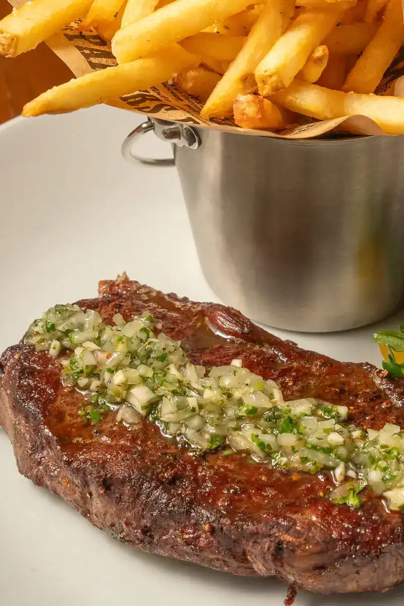 Grilled sirloin under chimichurri with a steel cup of fries