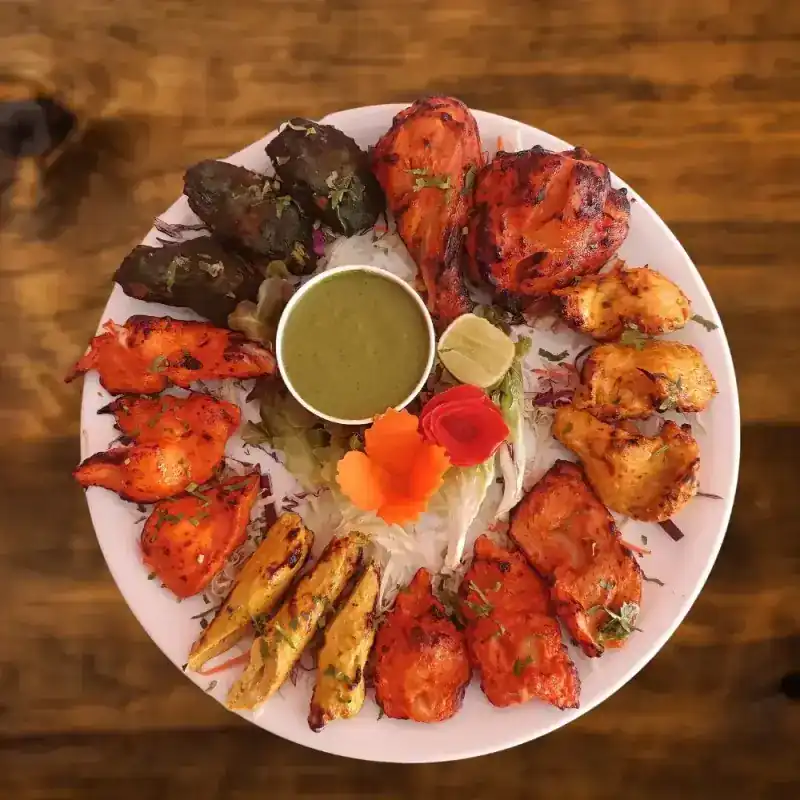 A round platter of tandoori chicken, kebabs and tikka around mint sauce
