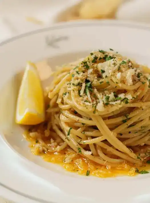 Spaghetti with anchovy, breadcrumbs and parsley, a lemon wedge beside it