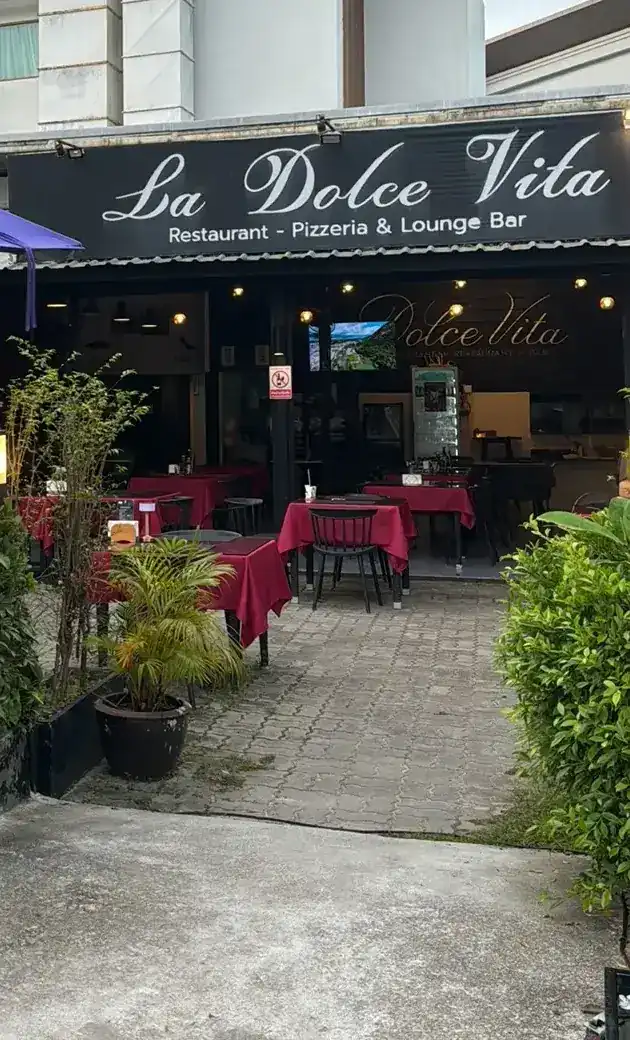 The front of La Dolce Vita: a black sign with the name in white script, and tables with red cloths