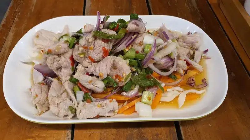 Spicy salad of sliced meat with chilli, red onion, green chilli and carrot on a white plate