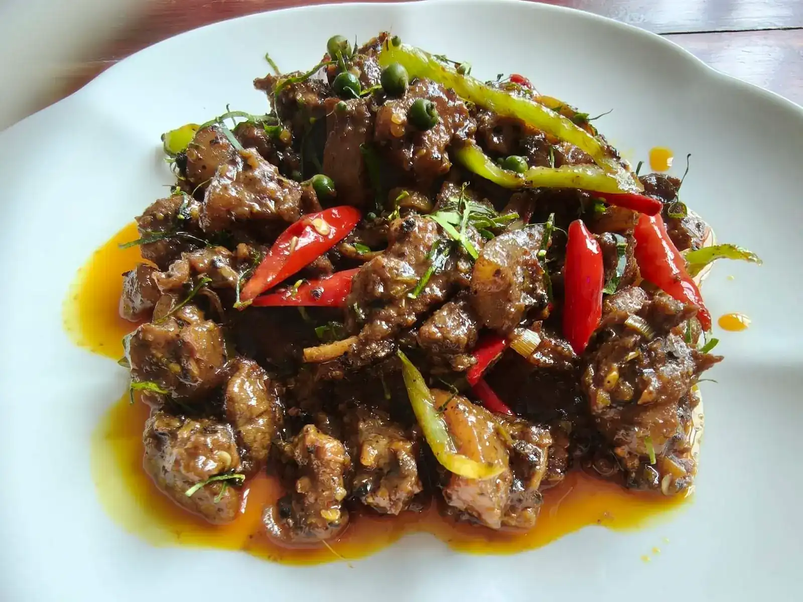 A spicy stir-fry with fresh red and green chillies and green peppercorns on a white plate