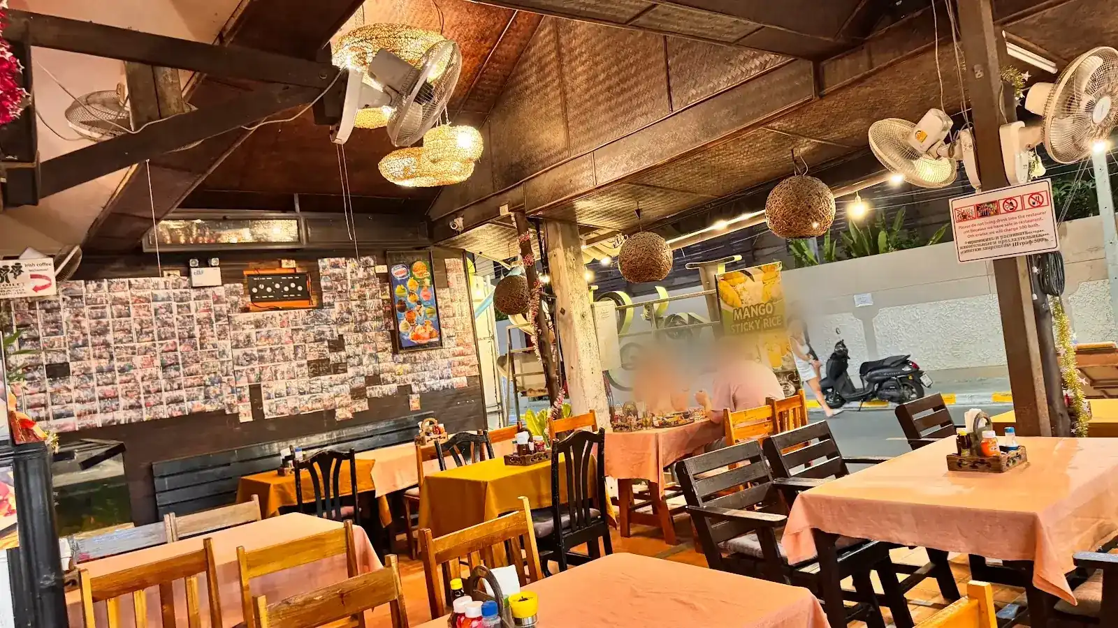 The open-sided dining room in the evening, with rattan lamps, fans and peach tablecloths