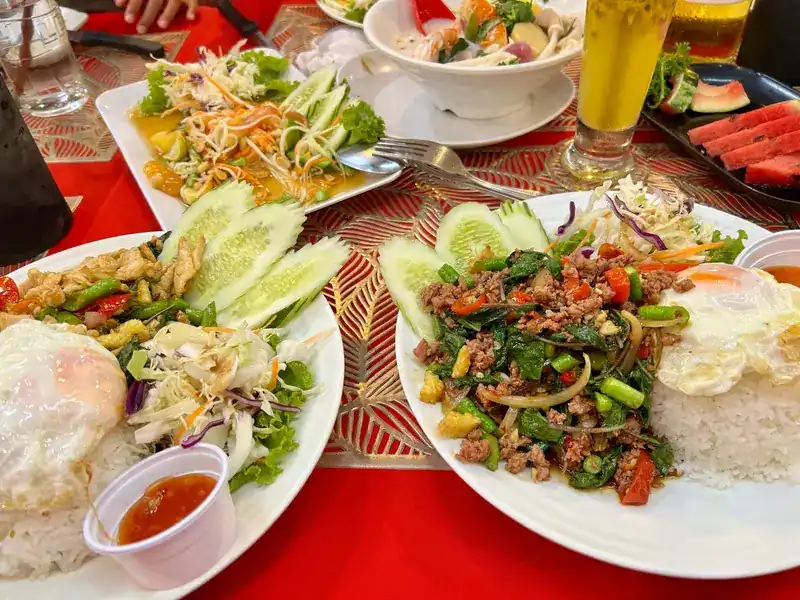Pad kra pao with fried eggs and rice, papaya salad and watermelon on a red table