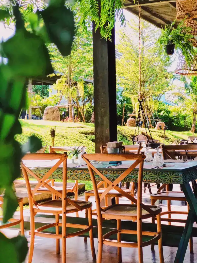 Wooden chairs at a carved teal table, looking out to the garden lawn