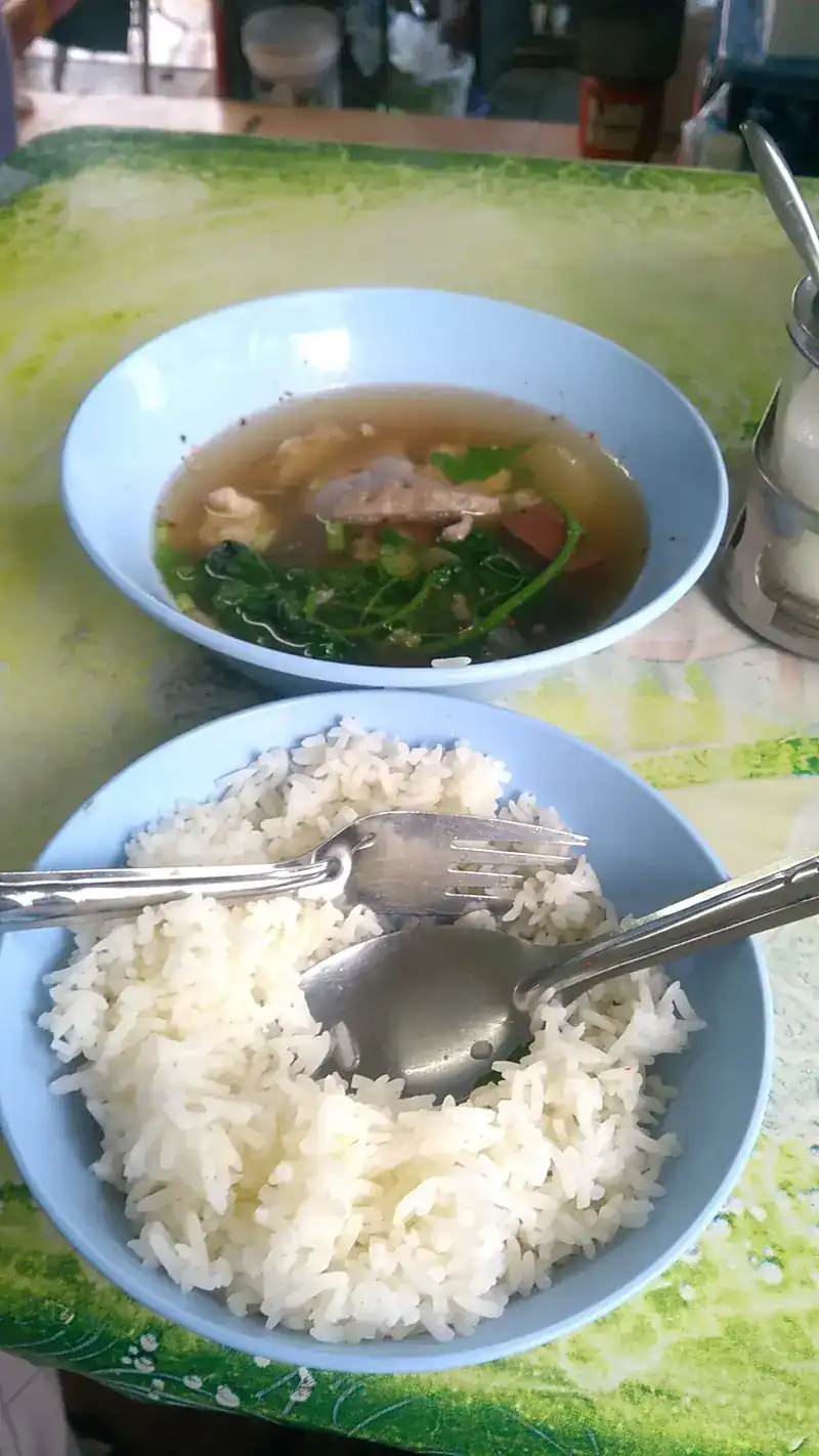 A blue bowl of clear soup with pork blood, pork and leafy greens, next to a bowl of rice