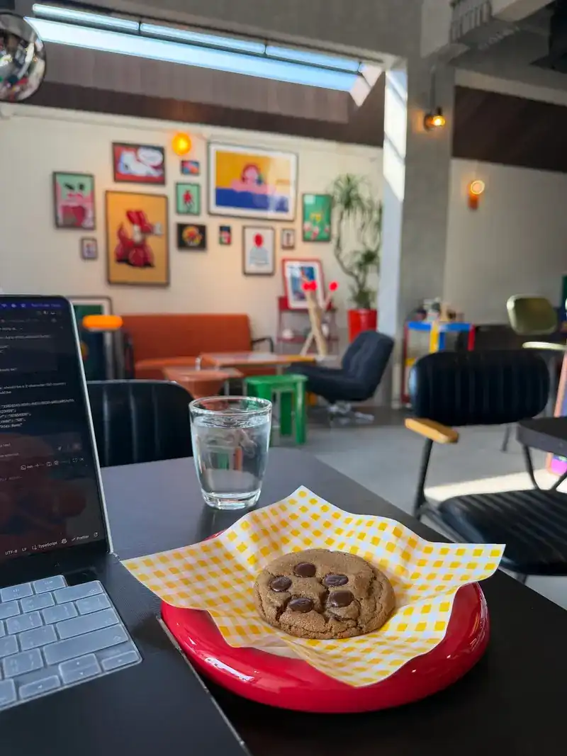 A chocolate chip cookie on a red plate, with the wall of colourful framed prints behind it