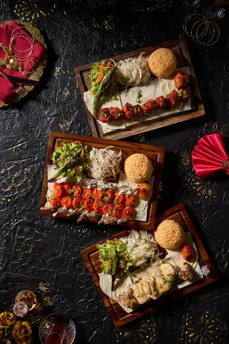 Three wooden boards from the grill, each with kebabs, salad, onions and rice