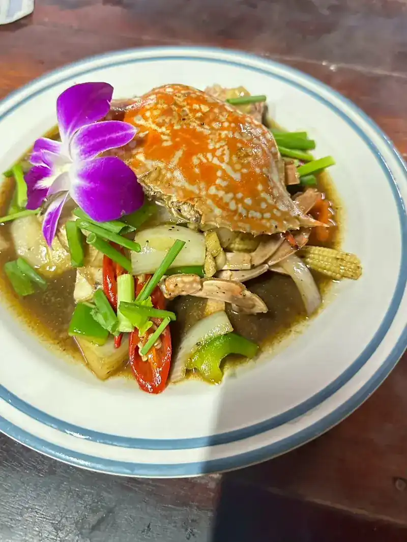 A whole crab with peppers, spring onion, onion and baby corn in sauce, garnished with an orchid