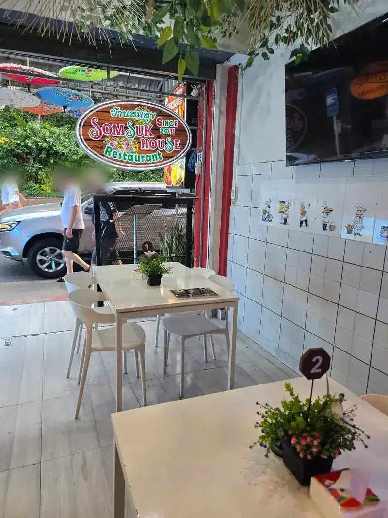Inside the open shopfront, looking out at the Somsuk House sign and painted parasols over the street / มองจากในร้านออกไปเห็นป้ายบ้านสมสุขและร่มวาดลายเหนือถนน