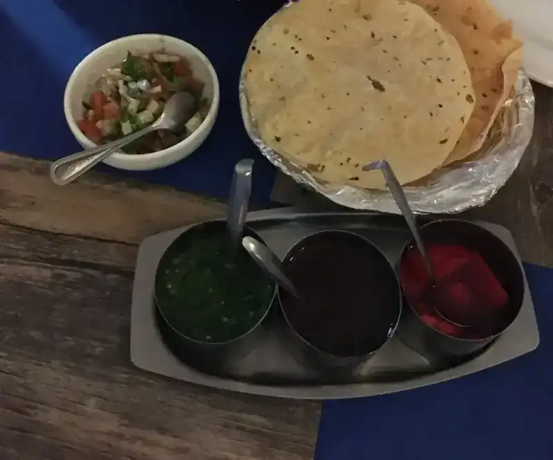 Papadums, a chopped salad and three chutneys on a steel tray