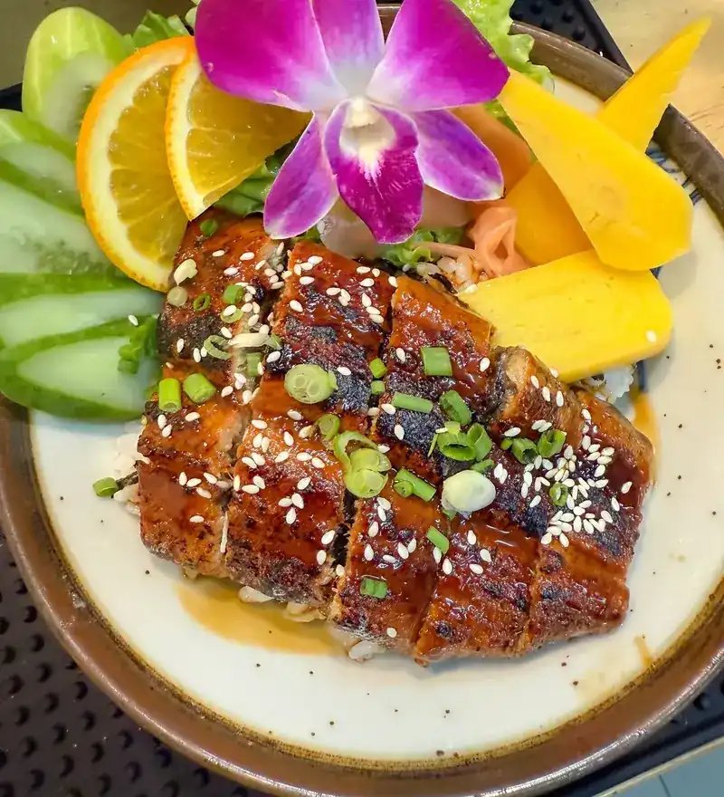 Eel rice bowl with sweet egg, cucumber, orange and an orchid