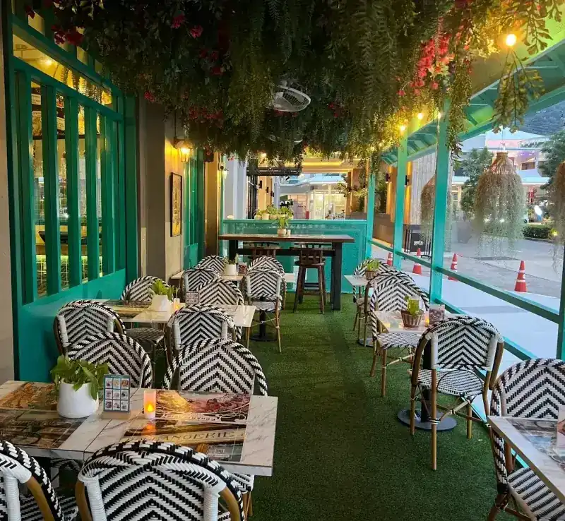 The terrace: black-and-white woven bistro chairs on green turf under hanging greenery