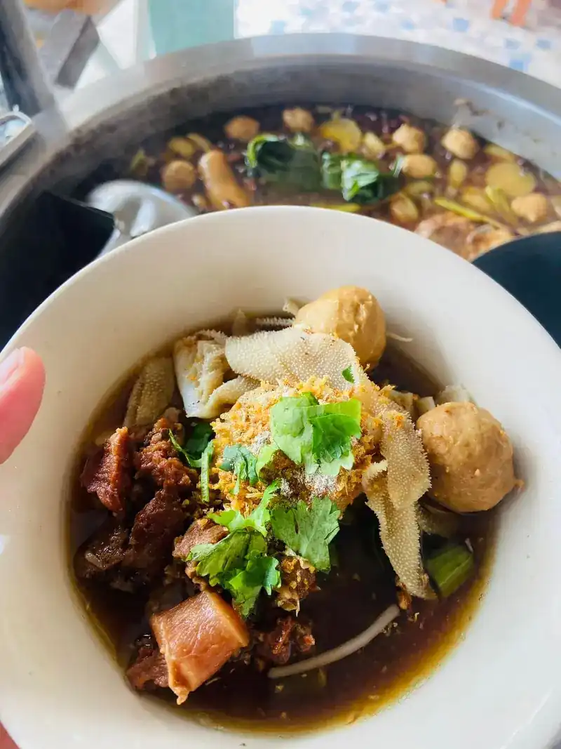 Bowl of noodle soup with braised beef, tripe, meatballs and coriander, the pot of broth behind