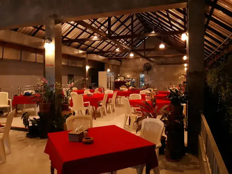 The dining hall in the evening: red tablecloths, white chairs and potted orchids under a beamed roof