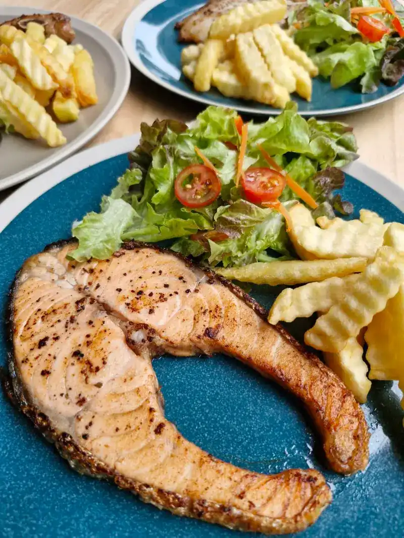 Grilled salmon steak with salad, cherry tomatoes and crinkle-cut fries on a teal plate