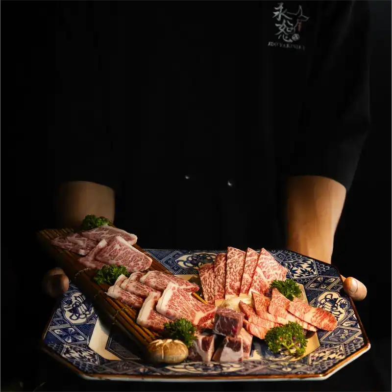 A cook in a black uniform holds out a blue-and-white platter of marbled beef cuts