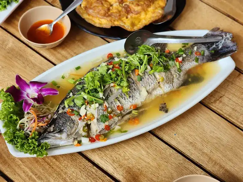 Whole steamed sea bass topped with chilli and coriander on a wooden table