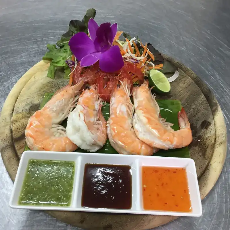 Prawns on a banana leaf with three dipping sauces and an orchid