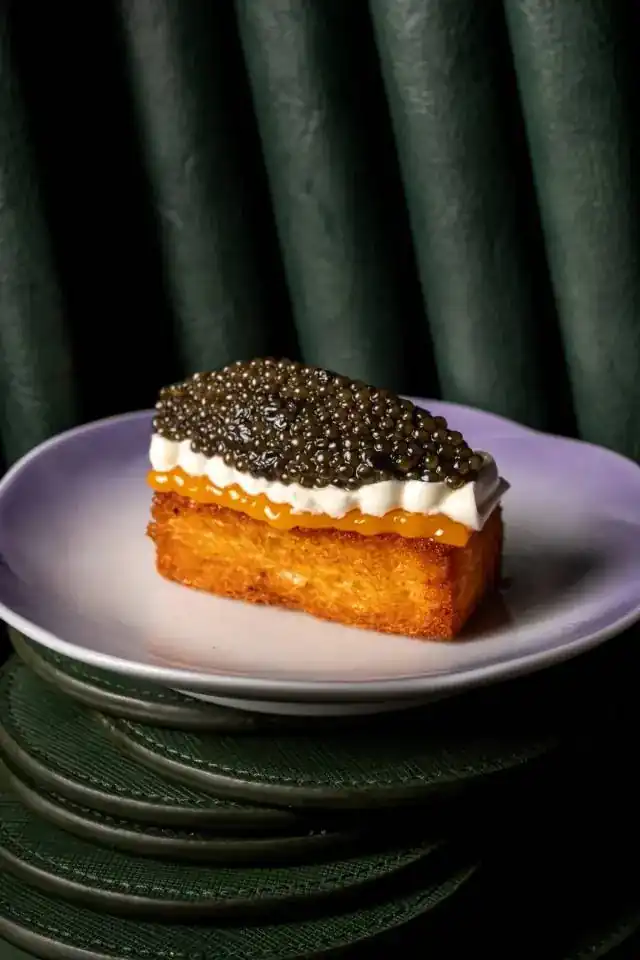 French toast topped with caviar, in front of a green velvet curtain