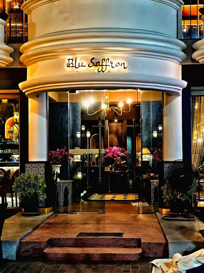 The entrance at night: a white, rounded front with the name lit above the glass doors and flowers inside