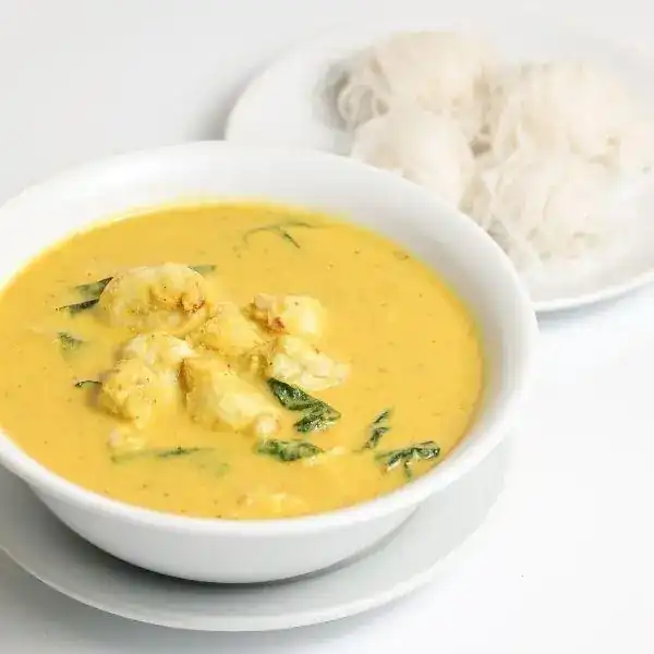 แกงเนื้อปูใบชะพลู: a bowl of yellow crab curry with a plate of rice noodles