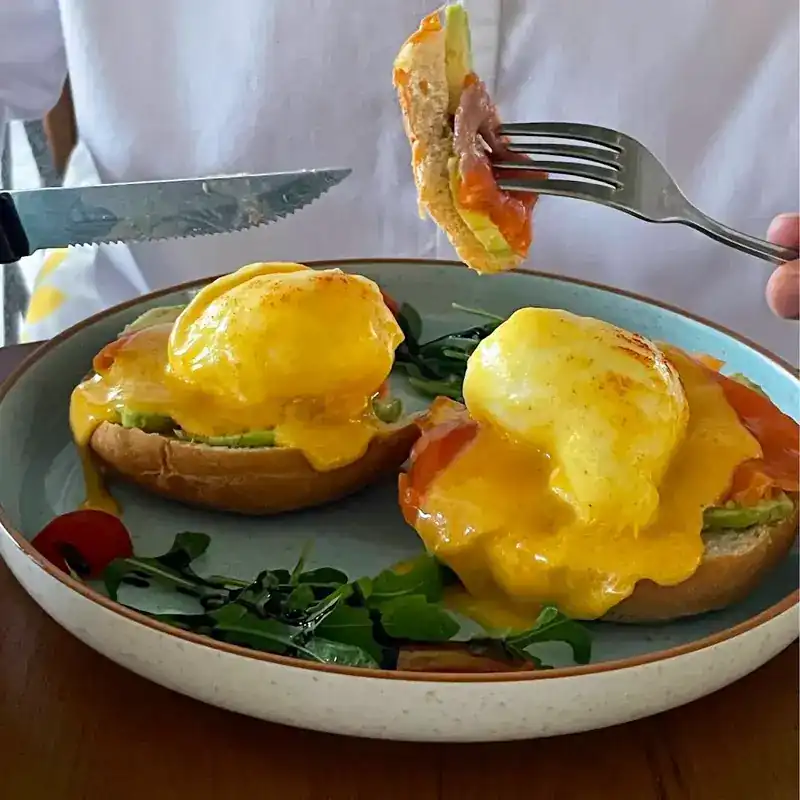Poached eggs and smoked salmon on toasted buns under hollandaise, with rocket