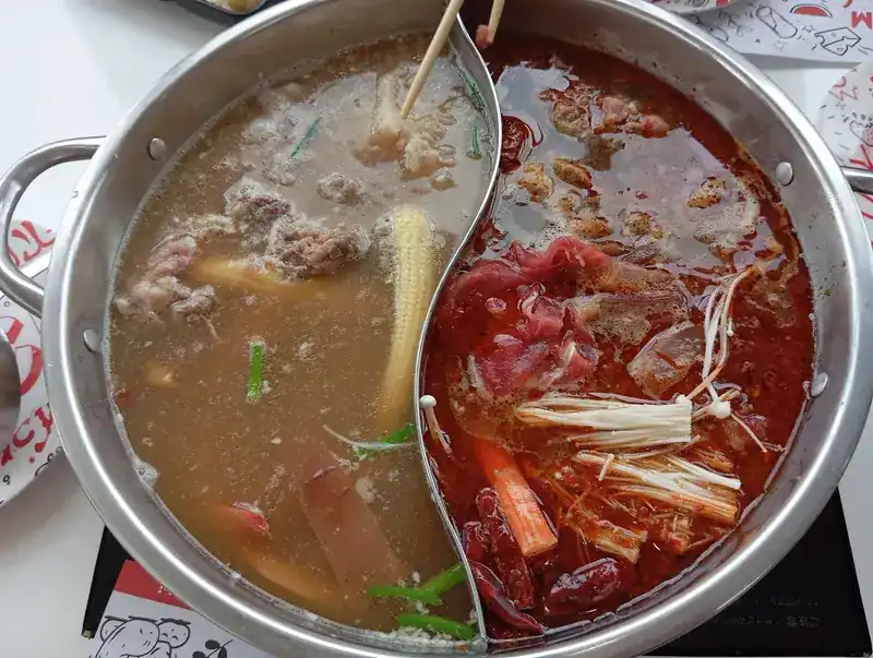 Clear and mala broth simmering with beef, baby corn and mushrooms