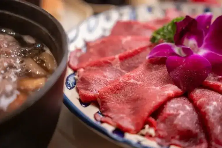 Slices of Wagyu beef with an orchid beside the hotpot
