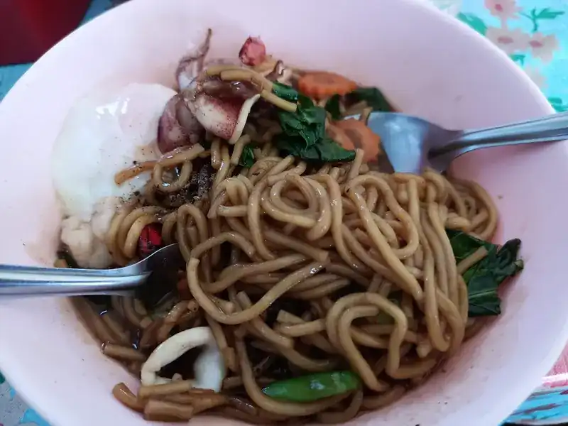 A bowl of thick yellow noodles with squid, greens and egg