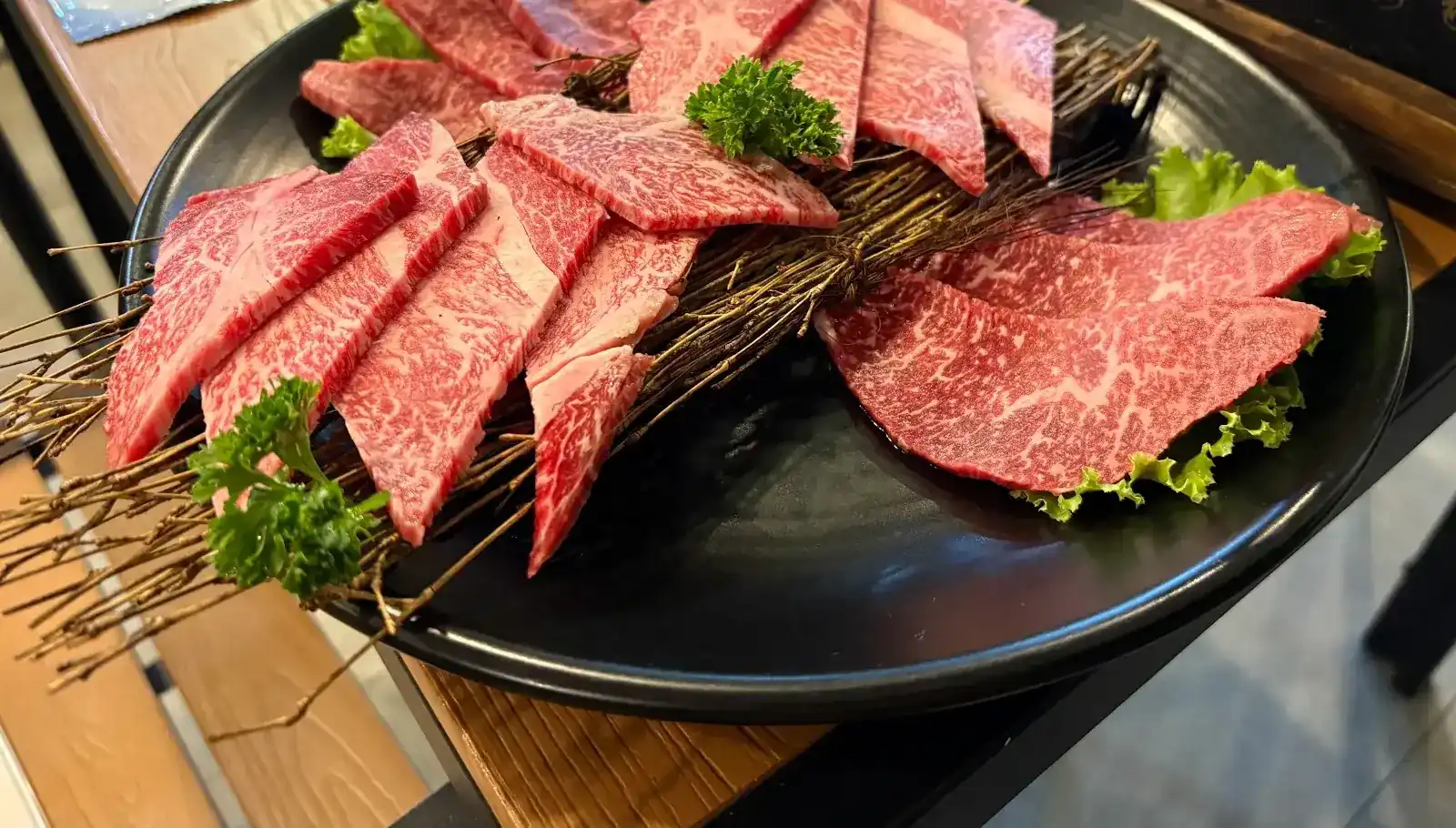 Raw marbled wagyu slices laid over a bundle of twigs on a black plate