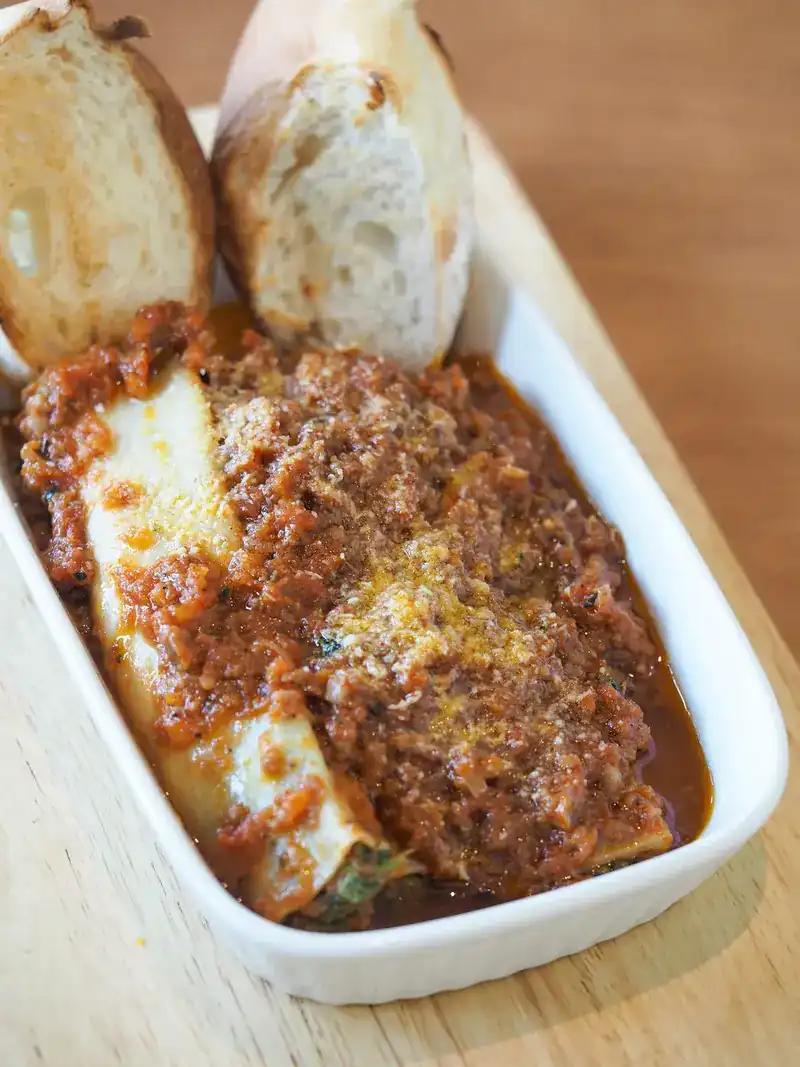 A baked filled pasta roll under meat sauce and grated cheese, with two slices of bread
