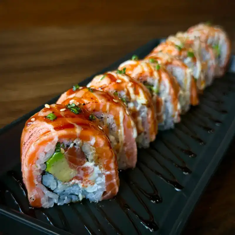 A salmon-topped maki roll with avocado inside, on a black plate