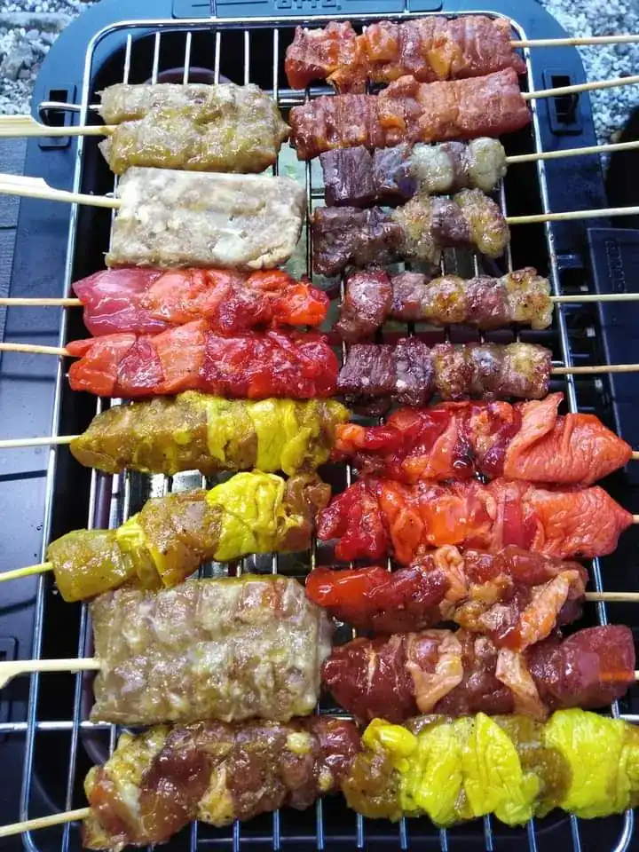 Two rows of skewers in yellow, red and dark marinades on a wire rack