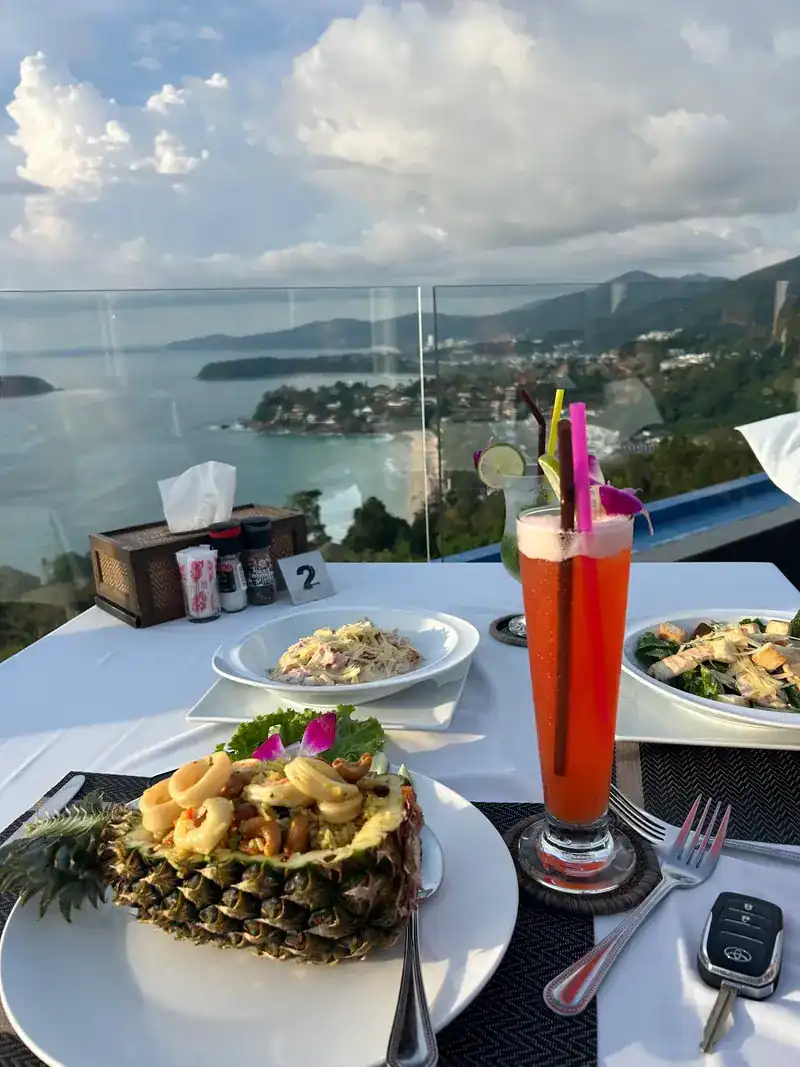 Pineapple fried rice and a tall red drink on a table by the rail, the bay behind / ข้าวผัดสับปะรดและเครื่องดื่มสีแดงบนโต๊ะริมราว มีอ่าวอยู่ด้านหลัง