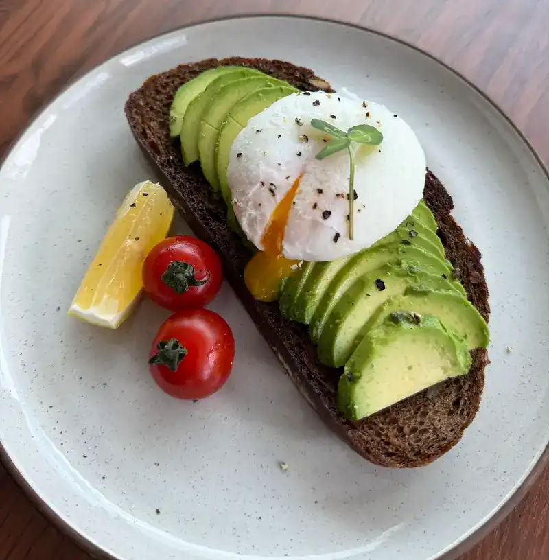 Avocado on dark toast with a poached egg, a lemon wedge and cherry tomatoes