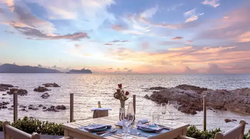 A table for two set above the rocks at sunset, the sea behind