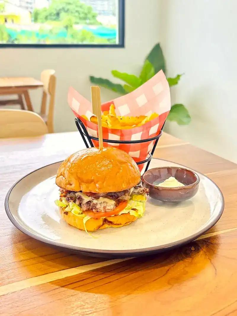 A burger on a brioche bun with a basket of fries and a small dip